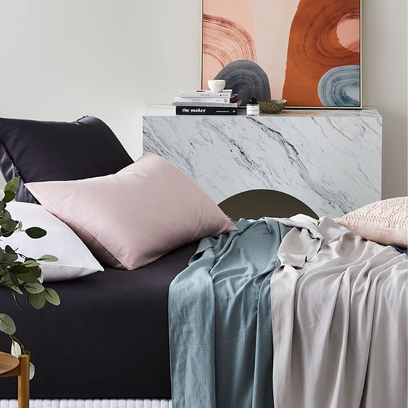 Bed displayed with bamboo linen set, bed sheets in black, quilt covers in shades of blue and grey and black white and pink pillows