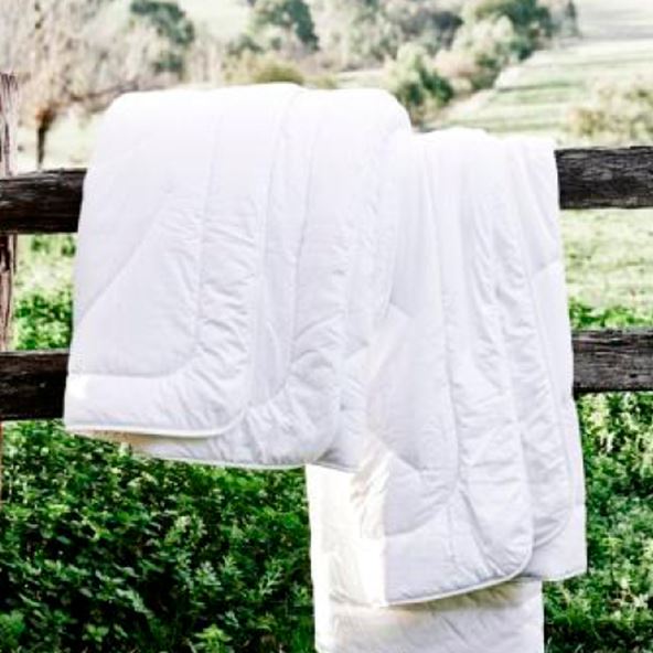 Outdoor setting white mattress protector placed hanging of a wooden fence, with a green nature background
