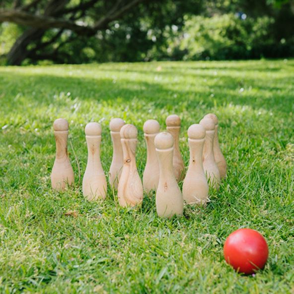 A backyard with lush green grass and a set of wooden bowling pins lined up ready to play. 