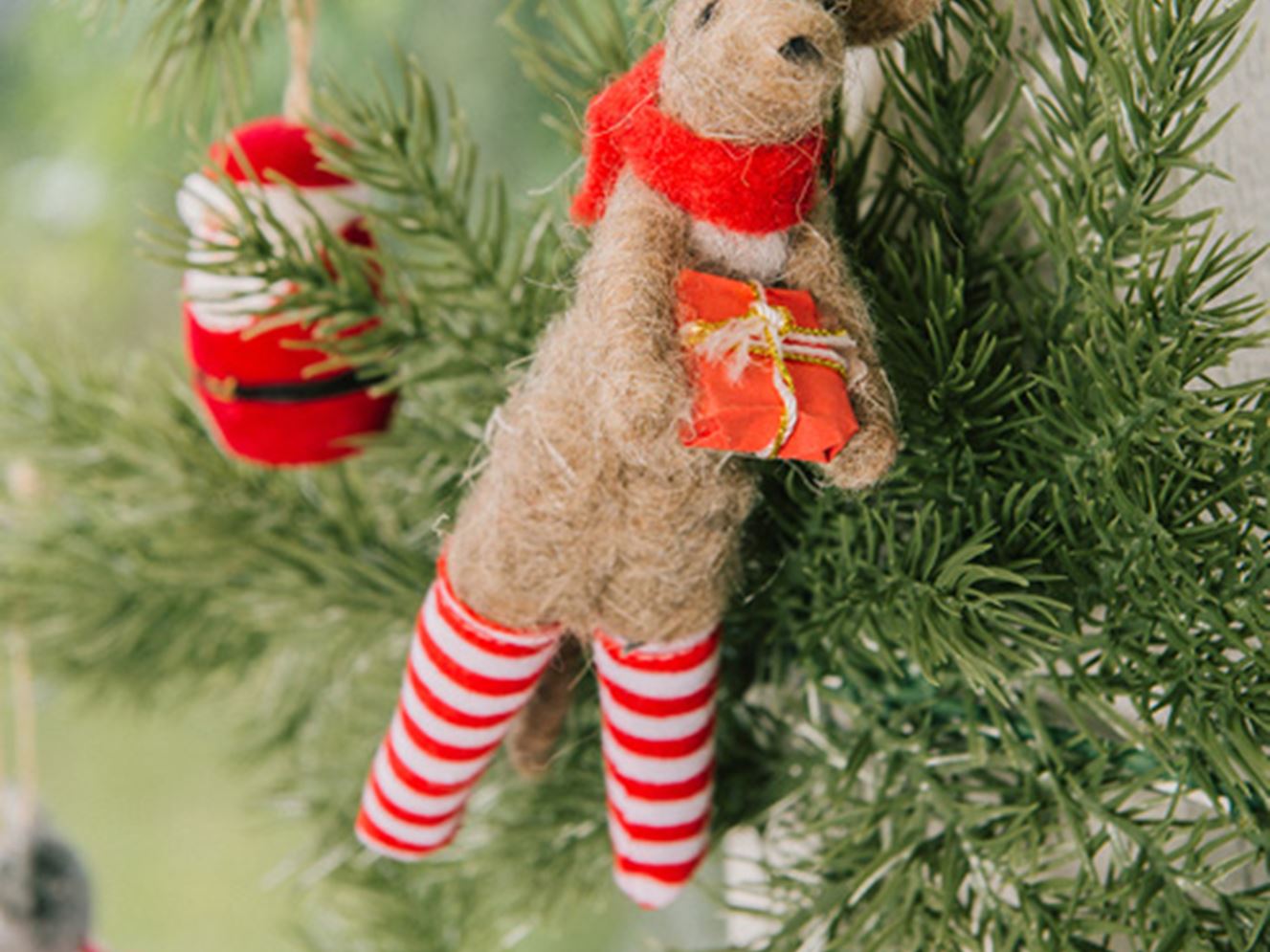 A close-up of a felt kangaroo Christmas decoration hanging on a green Christmas tree. 
