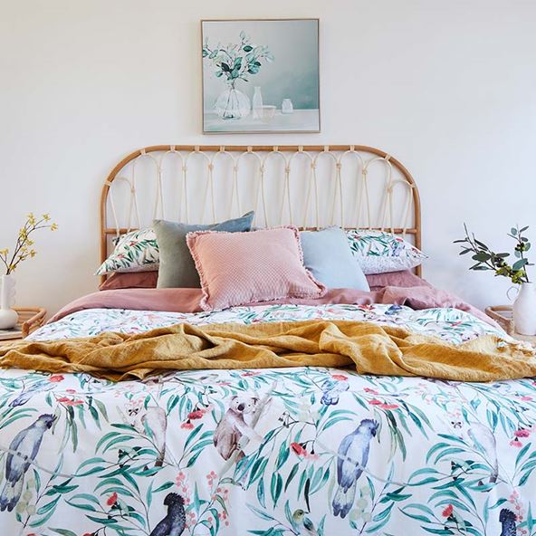 A vibrant botanical printed bedlinen styled with colourful linen cushions and a natural rattan bedhead. 