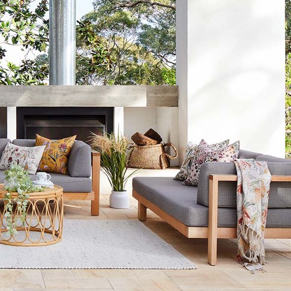 Outdoor seating area with couches, a fireplace and styled with a rattan table, soft rug, native cushions, and throw. 