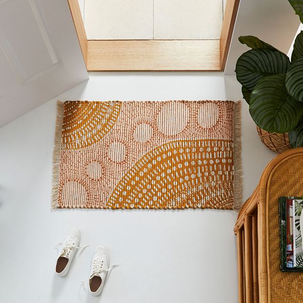 A door mat lies near a doorway, showcasing the Indigenous artwork of the Brad Turner collection in earthy tones.