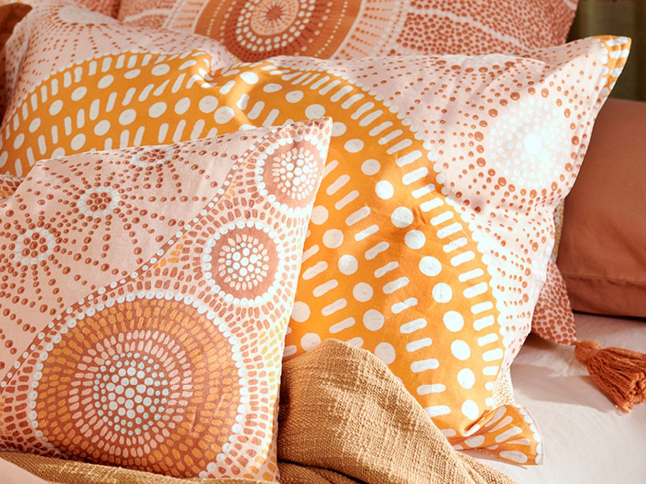 Close-up shot of the beautiful patterns on the pillowcases available in the collection, showcasing the Indigenous artwork of Brad Turner with vibrant orange against pastel hues of earth, pink and yellow. 