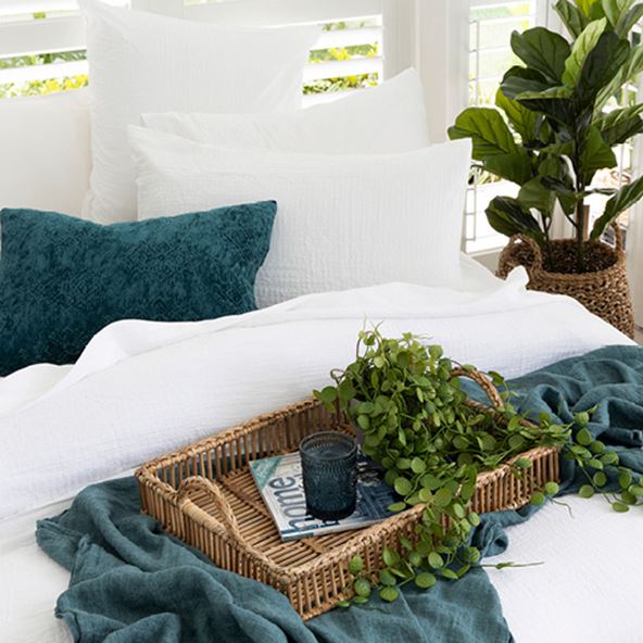 Close-up of tray styled on top of a white bedlinen and navy linen throw with a pot plant in the background. 