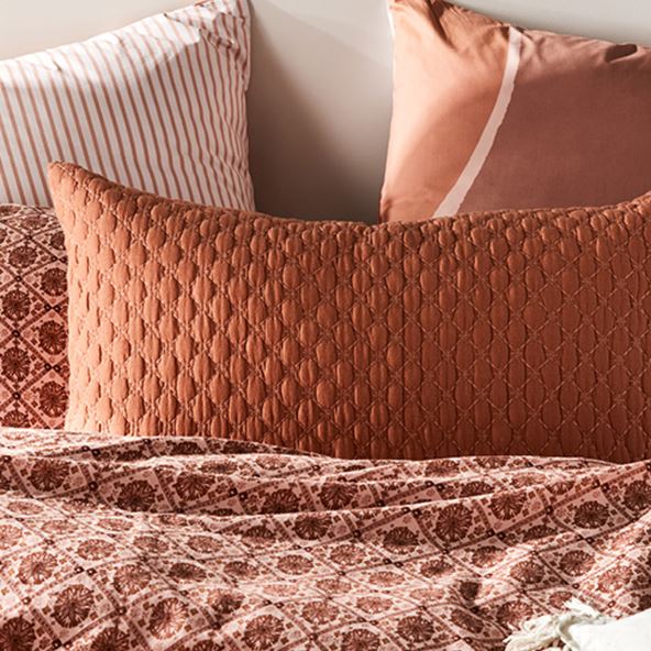 Pillows in a range of terracotta hues, soft and dark pinks leaning on each other on the wall at the top of a bed.  