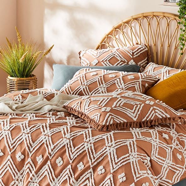 Terracotta bedlinen with textured tufting in diamond patterns on a bed with a rattan bedhead and colourful accessories. 