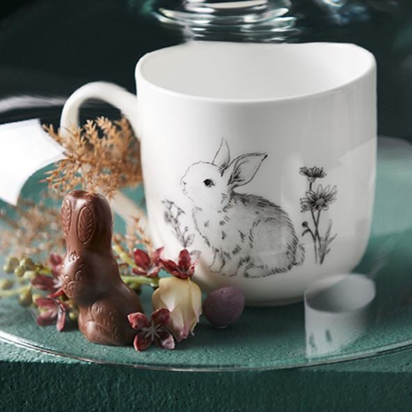 Fleur Harris x Adairs Easter Mug featuring a bunny drawing styled on top of a plate with a chocolate bunny and floral stem. 