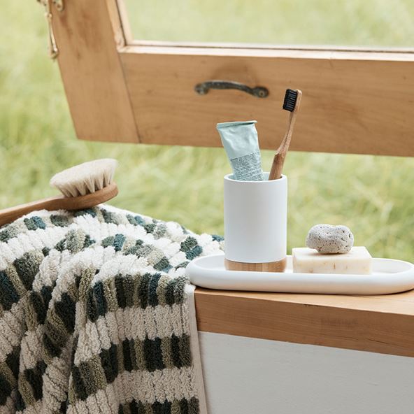 A green patterned towel and a small marble tray filled bathroom accessories sits on a window sill in front of the slightly ajar window.