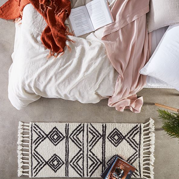 Bird’s eye view of bed styled with Vintage Washed Linen in Linen and Nude Pink, and a rug with tassels at the side of the bed. 