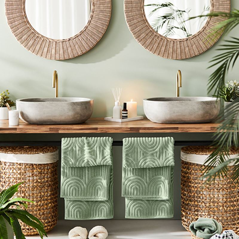 Bathroom styled with green textured towels, rattan laundry baskets, and greenery. 