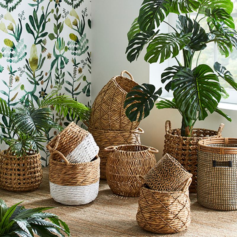 Selection of stacked rattan baskets on top of a rug, and some with plants inside. 