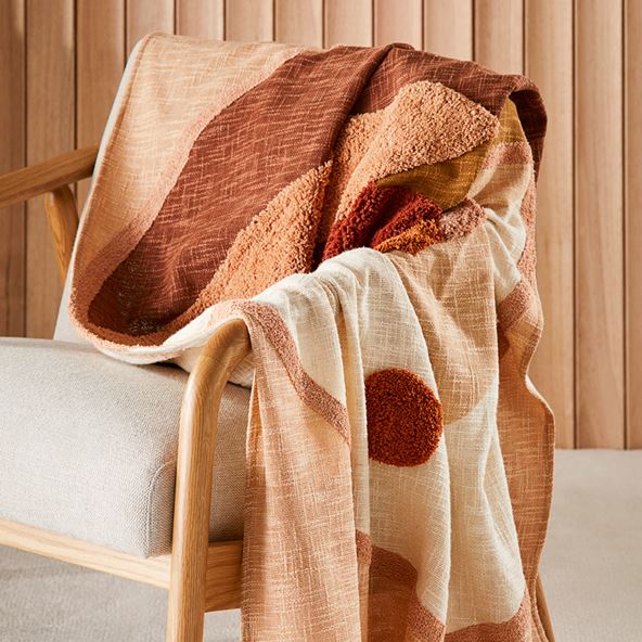 An armchair with a textured throw draped over the arm. The background is slatted wooden wall.