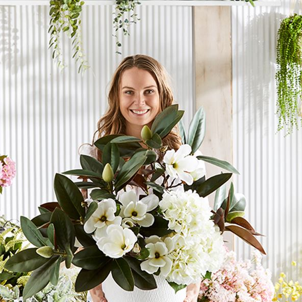 Woman in smiling holding a large selection of statement flowers and leaves.