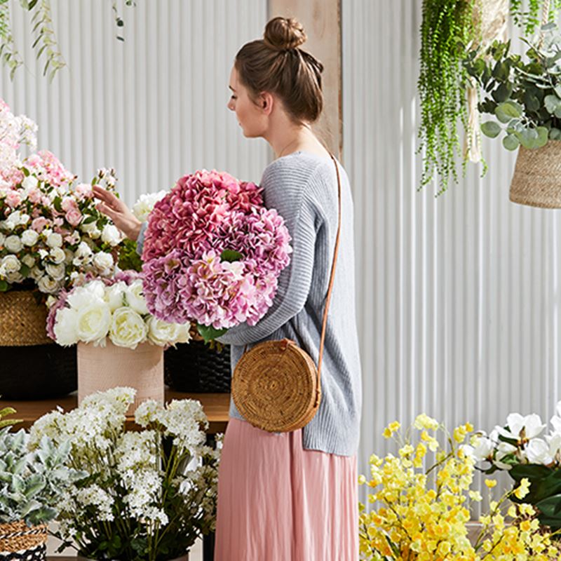 Woman is seen carefully selecting her flowers, she is holding a bouquet of pink toned flowers.