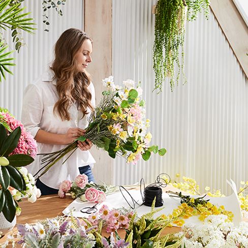 Woman is seen at a table curating her bunch of  colourful flowers and stems.