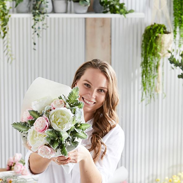 Woman smiles while holding a beautifully curated bunch of posies, in the light shades of pink and white.
