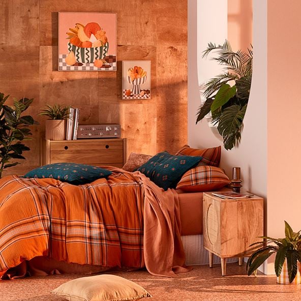 A bed shot from the side, with orange check bedlinen and an assortment of printed cushions.