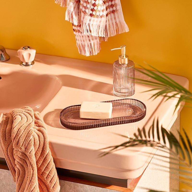 A shot of the corner of a vanity, with glass bathroom accessories and textured towels in orange shades.