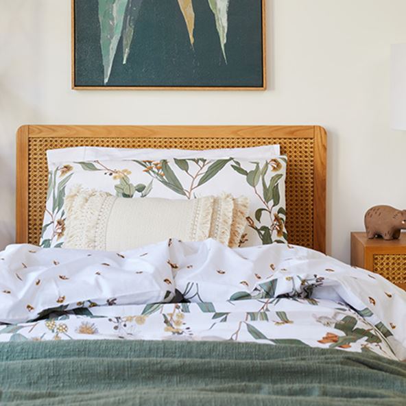 Close-up of kids’ bed with botanical bedlinen, linen green throw, tufted cushion, and Arden Rattan Bed and Side Table. 