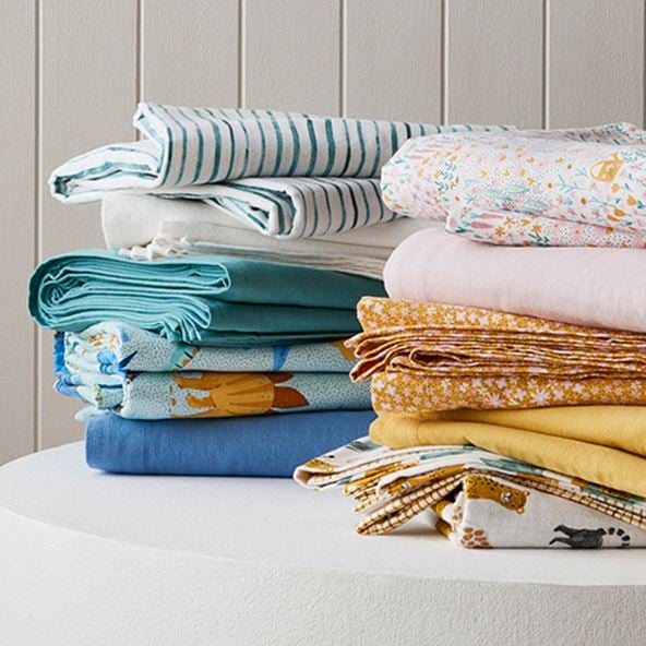 Two stacks including printed, plain and patterned kids flannelette sheets sitting next to each other on a white round table. 