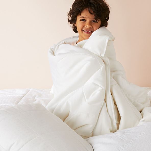Child sitting up on a bed, cuddling a warm quilt around them, surrounded by pillows. 