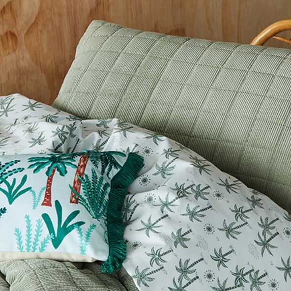 Close-up of quilted kid’s bedlinen with reverse a palm tree print, styled with a matching fringed cushion.