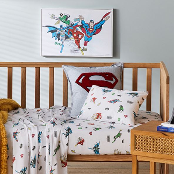 Side-on-view of cot with Justice League Cot Sheet Set, matching pillowcase, cushion (for display only) and wall art. 