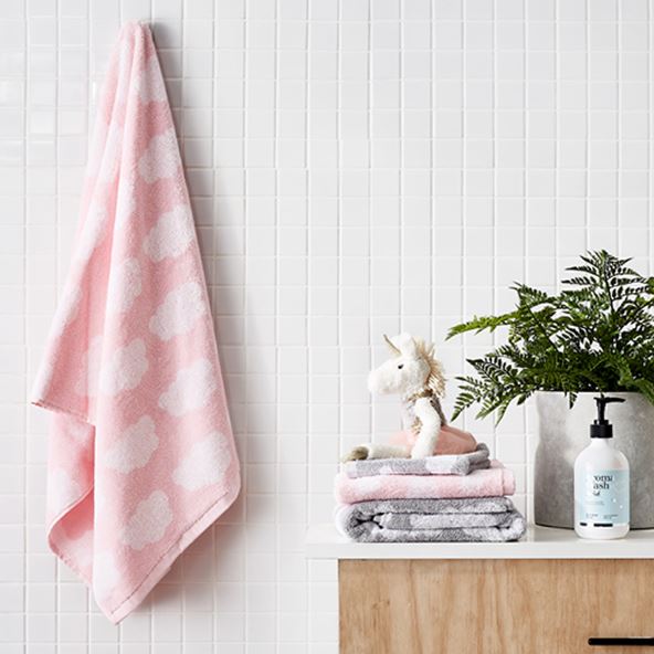 Baby cloud pink bath towel hanging in bathroom next to stack of matching towels, unicorn plush toy and kids aroma wash. 