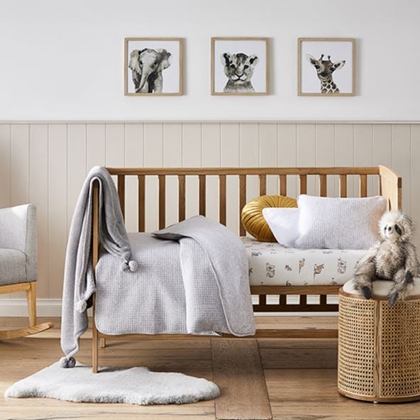 Nursery with an Arden Natural Rattan Cot styled with a matching side stool, printed fitted sheet, cot quilt and accessories. 