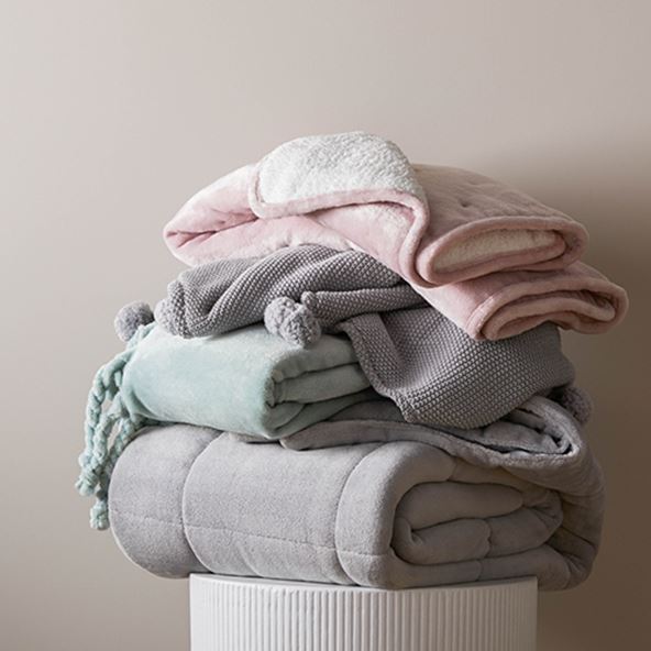 A stack of plush, fleecy, textured and tasselled baby blankets sitting on top of a round ribbed white table. 