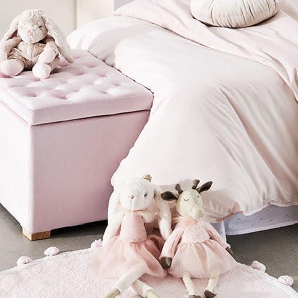 various pink themed plush toys for kids leaning against a pink themed bed with bed sheets, storage chest and pink rug