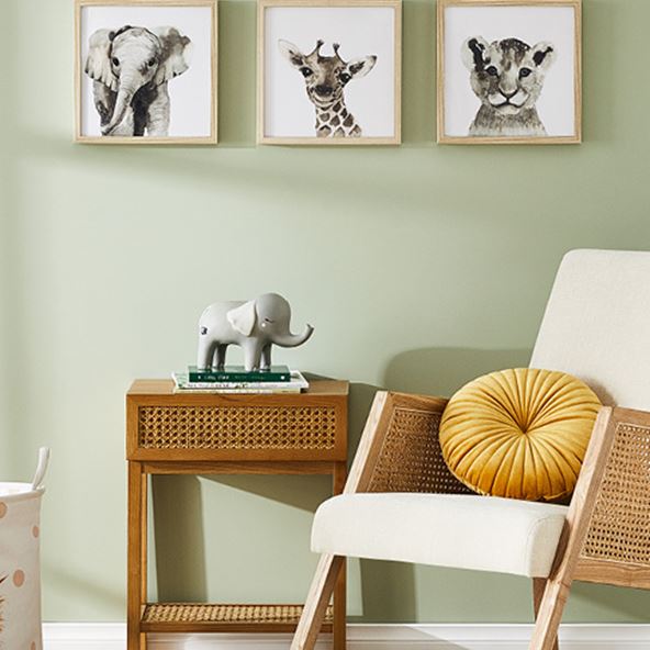 A rocking chair and side table next to a green wall featuring safari wall art with an elephant, giraffe and tiger.