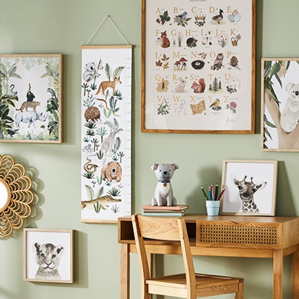 A green wall featuring wall art in natural frames with a kid’s desk and matching rattan chair situated against the wall. 