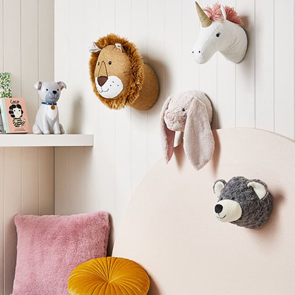 3D plush wall art including the face of a bunny, bear, lion and unicorn on a wall above a children’s reading nook. 