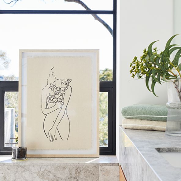 Wall art sitting on a bathroom ledge in a wooden frame featuring a sketch of a lady. 