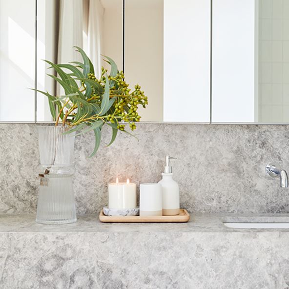 Marble bathroom countertop with bathroom tray and matching accessories, plus a candle and glass vase. 
