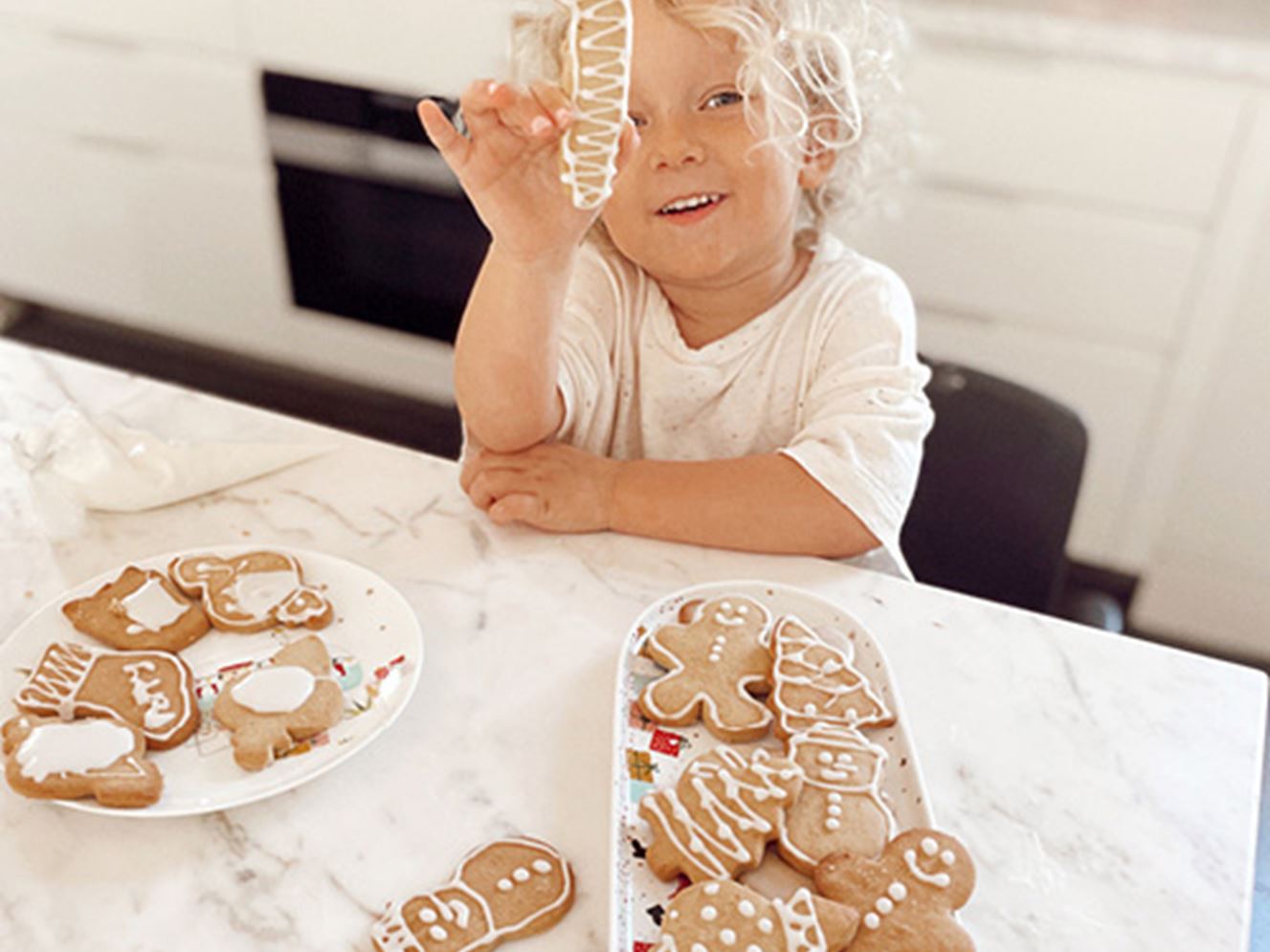 Toddler at kitchen bench with plate of Christmas gingerbread cookies. 