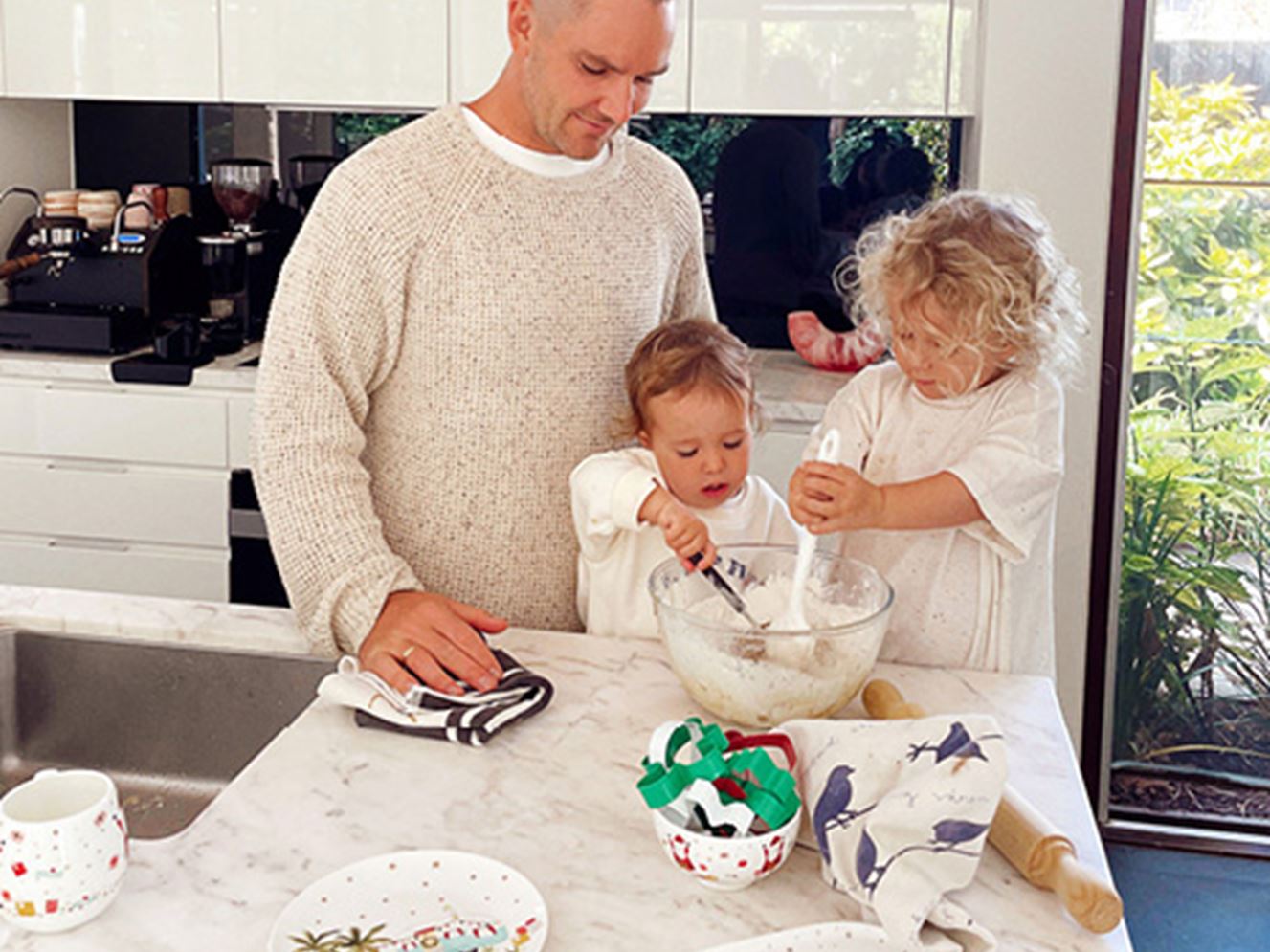Father with two young children baking Christmas gingerbread cookies at kitchen bench.
