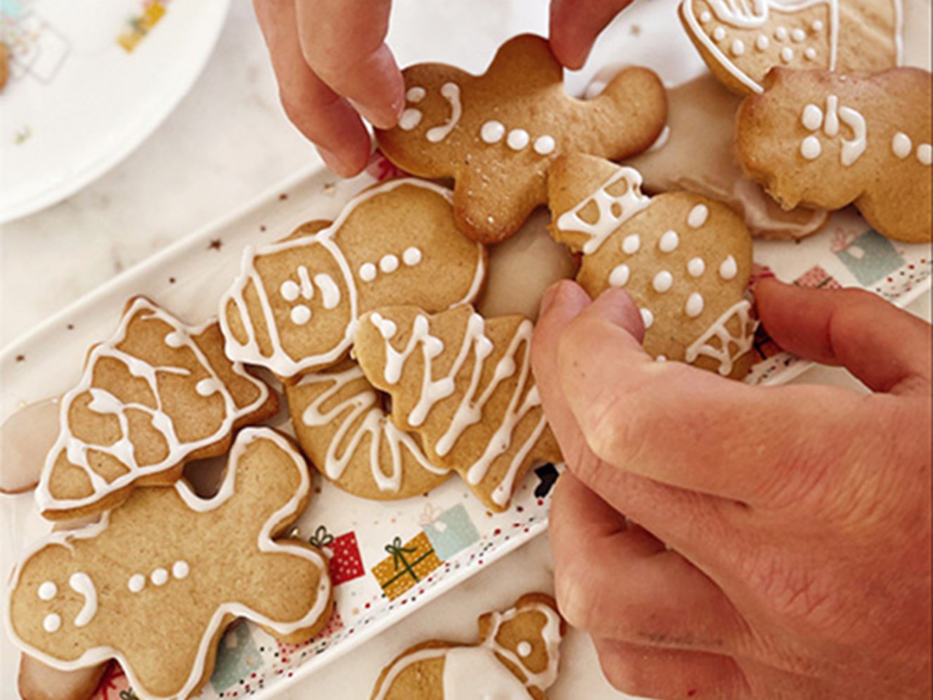 Hands arranging Christmas gingerbread cookies onto a Christmas plate