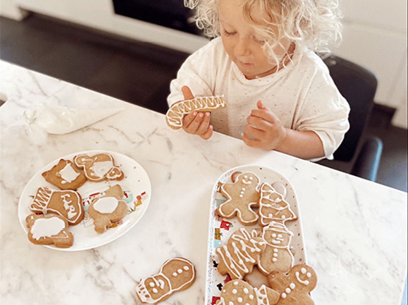 Toddler at kitchen bench eats a Christmas gingerbread cookie.