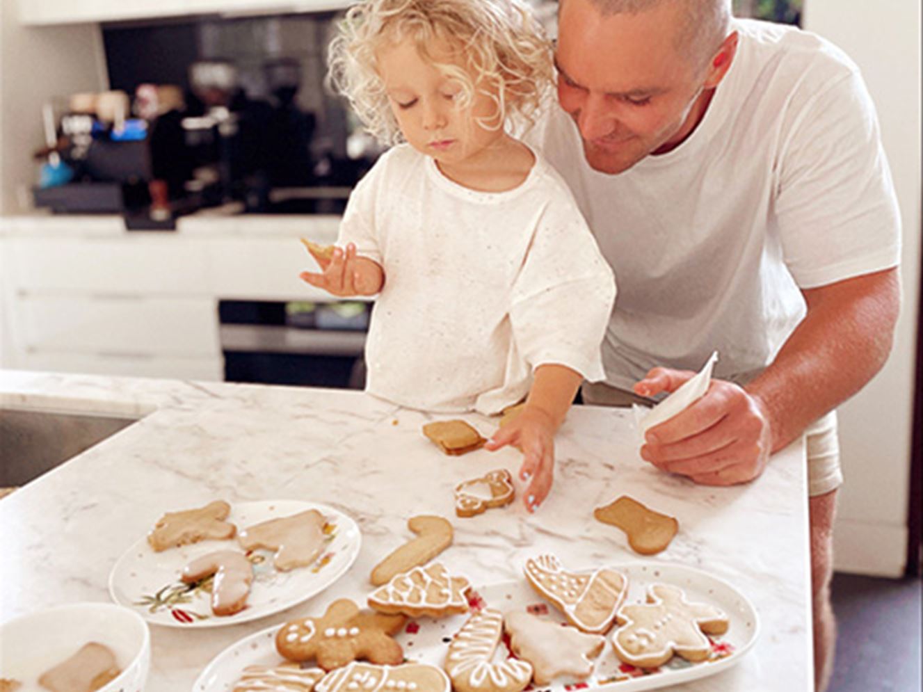 Father and toddler standing at a bench decorating Christmas gingerbread cookies.