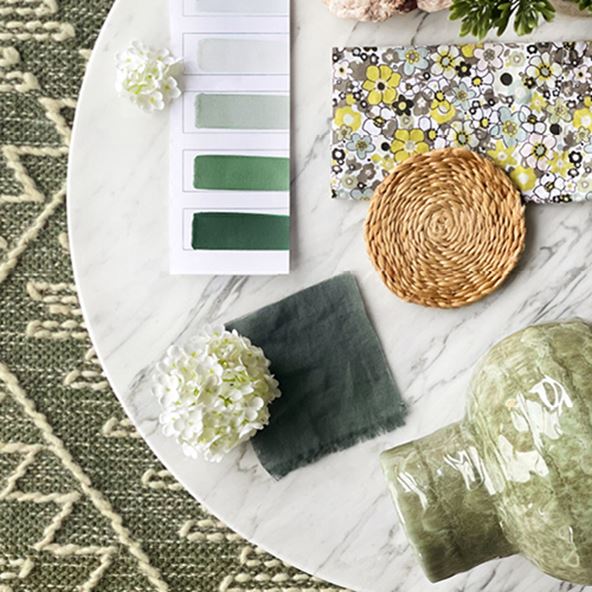 Bird’s eye view of a marble table with a green textured rug underneath. On top sits swatches including in green and a floral swatch.