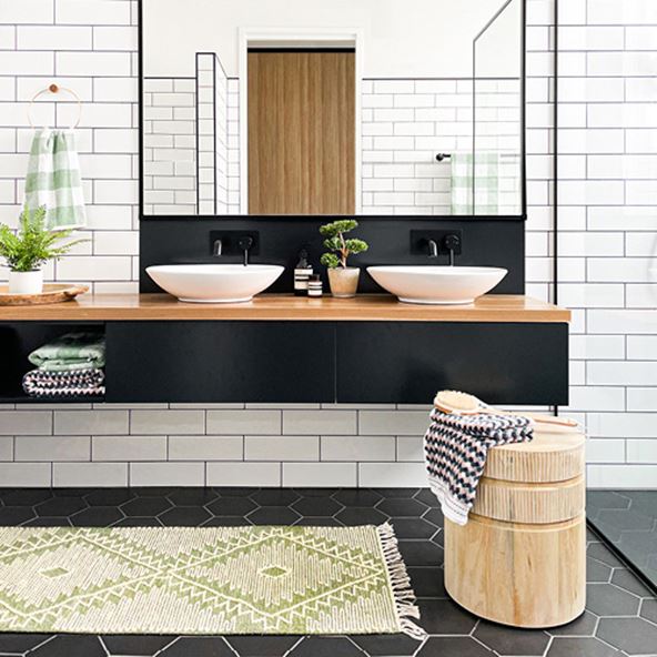 Bathroom with black and natural vanity, white tiles and two white basins styled with long green and white rug in front.