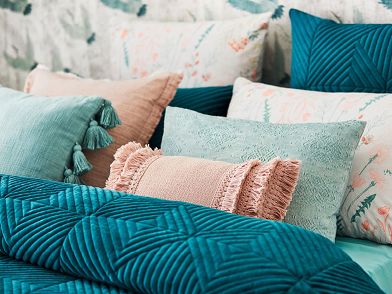 Various pillows with teal, pink and floral tones placed on the bed