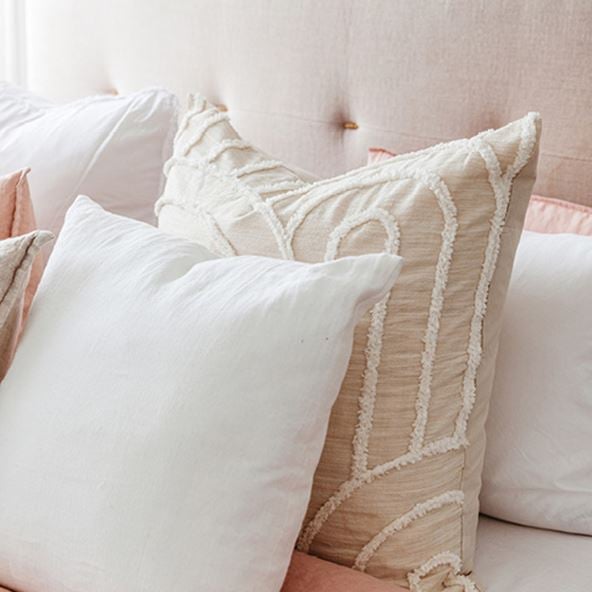 Close-up of two European pillows – one in white and one in a neutral linen colour with white textured detailing. 